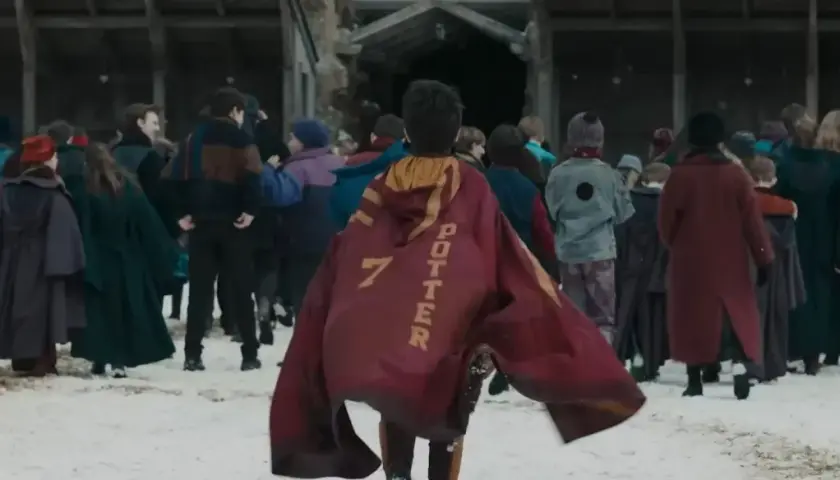 Chłopiec w pelerynie z napisem "POTTER 7" idzie przez śnieg w otoczeniu innych uczniów, jak w serialu Harry Potter.
