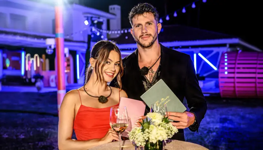 Para z Love Island, która wygrała, pozuje z uśmiechem. Ona w czerwonej sukience, on w czarnym garniturze.