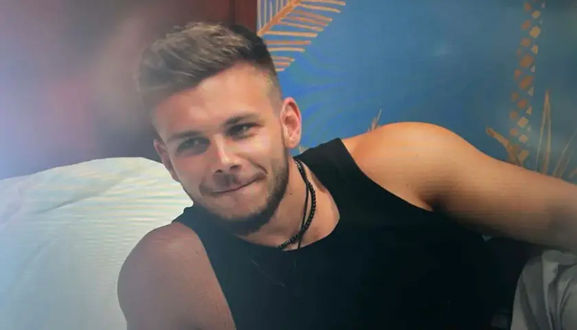 Bartek z Hotel Paradise, z uśmiechem na twarzy, w czarnej koszulce, na tle tropikalnej tapety.