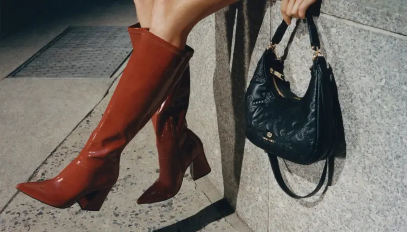 Kobieta w czerwonych kozakach i czarnej torebce z logo Nine West. Nine West to znana marka obuwia i akcesoriów.