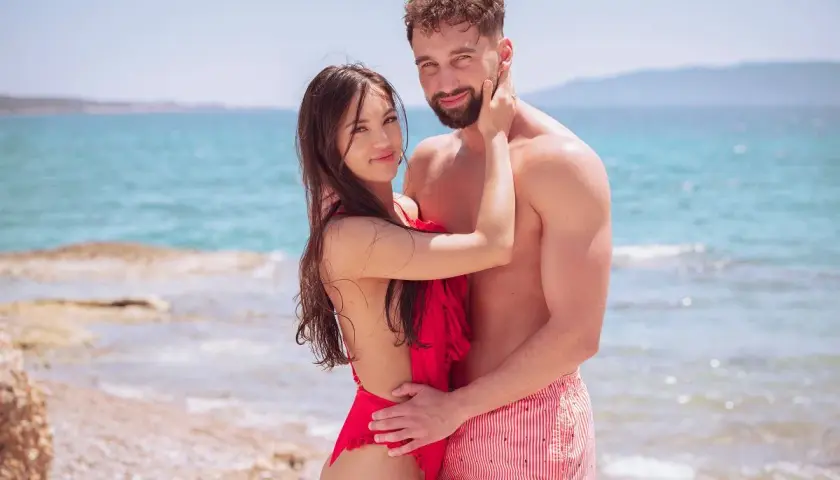 Para zakochanych na plaży, w objęciach, z morzem w tle. Ich spojrzenia mówią wszystko, bo love never lies.