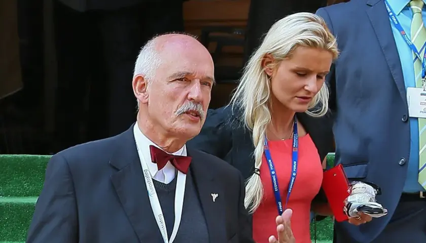 Janusz Korwin-Mikke z wąsem i w muszce, obok niego kobieta w czerwonej sukience. Może to jego dzieci?