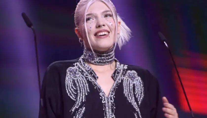 Daria Zawiałow w błyszczącej kreacji, z błyszczącymi ozdobami na twarzy, uśmiecha się na scenie.
