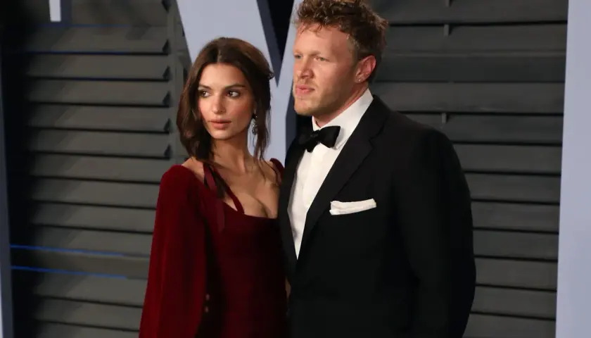 Sebastian Bear McClard w czarnym smokingu z muszką i białą poszetką, obok kobiety w czerwonej sukni.