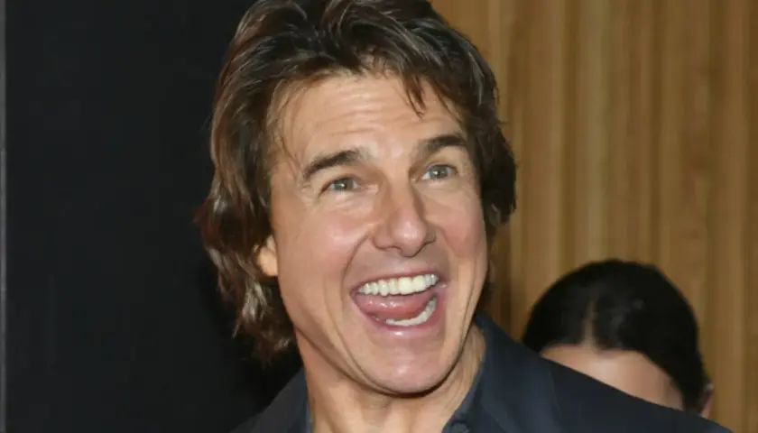 Uśmiechnięty Tom Cruise, którego twarz przypomina scenę z filmu o sekcie, z szeroko otwartymi ustami i widocznymi zębami.