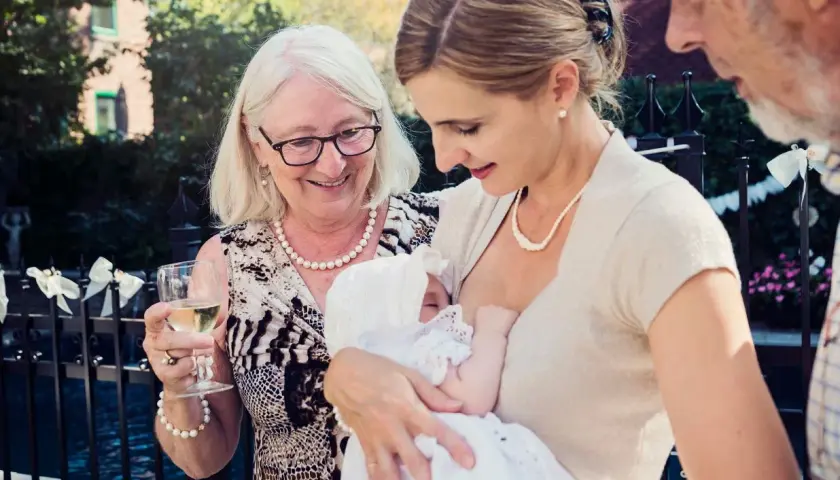 Elegancka stylizacja na chrzciny: matka karmi dziecko w białej sukience, babcia z kieliszkiem wina, dziadek obok.