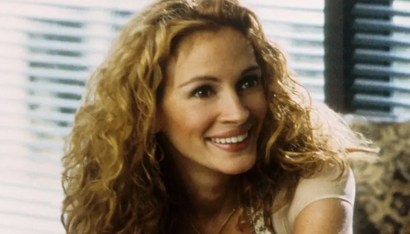 Julia Roberts z burzą blond loków, uśmiechnięta, jakby opowiadała historię z filmów na faktach.