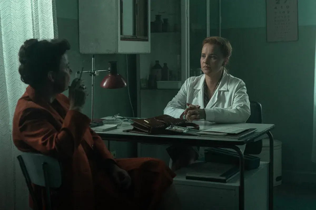 Dwie kobiety w gabinecie lekarskim. Jedna w białym kitlu, druga w pomarańczowym płaszczu, pali papierosa. Czy to scena z filmu "Ołowiane dzieci" czy na faktach?