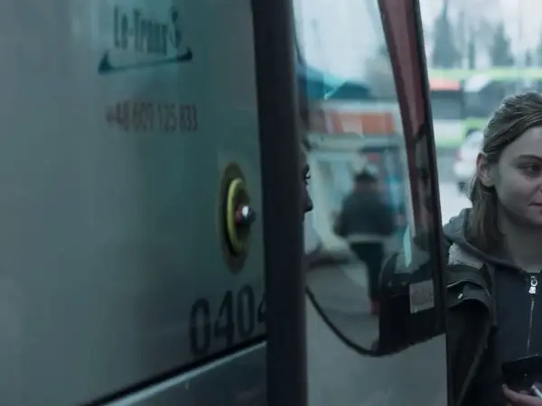 Młoda kobieta patrzy w lustro autobusu, marząc, by jak najdalej stad.